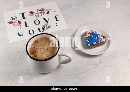 Tazza di caffè, pan di zenzero a forma di cuore e una valentina con la parola Ti voglio bene. Colazione di San Valentino. Concetto di San Valentino. Messa a fuoco morbida Foto Stock