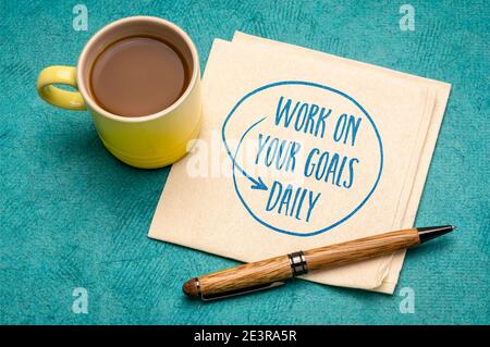 lavori sui vostri obiettivi giornalieri - promemoria motivazionale, handwriting su un tovagliolo con una tazza di caffè, l'impostazione di obiettivo, il commercio e lo sviluppo personale concep Foto Stock