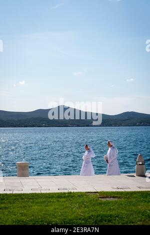 Due monache cattoliche romane vestite di vestiti bianchi che camminano sul lungomare nella città vecchia, Zara, Dalmazia, Croazia Foto Stock