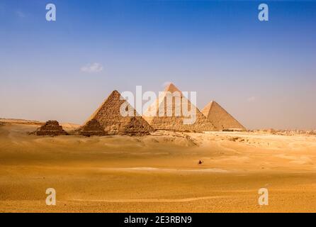 Nord Africa Egitto Cairo Giza uomo di città in sella a cammello di fronte alle piramidi d'Egitto nel paesaggio desertico piramidi cielo blu della città di giza Foto Stock