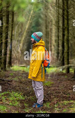 Uomo che indossa impermeabile giallo e zaino in piedi nella foresta Foto Stock