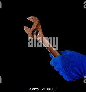 La mano di un uomo in un guanto blu contiene una chiave arrugginita. Primo piano Foto Stock