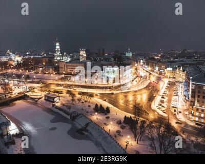 Inverno sera illuminato paesaggio aereo della città con fiume ghiacciato nevoso. Terrapieno di Lopan, Cattedrale della Dormizione, Serhiivskyi Maidan a Kharkiv, Ukrain Foto Stock