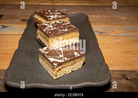 Un delizioso mucchio di Millionaires Flapjacks cioccolato e toffee dolce prelibatezze su un tavolo di legno Foto Stock