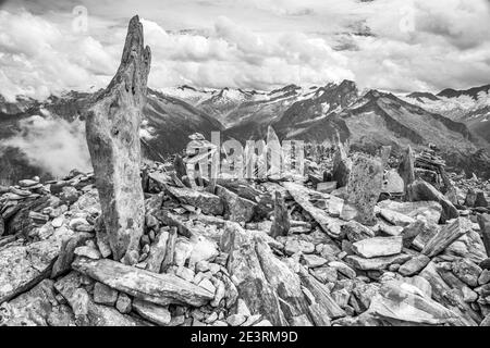 Immagini drammatiche di montagna in monocromo delle montagne delle Alpi Zillertal nel Tirolo austriaco, qui viste guardando attraverso il grande vuoto sopra Schlegeis fino all'Hochfeiler e Grosser Moseler dalla piccola vetta di Peterskopfl sopra il rifugio Friesenberberg Haus, dove ci sono molti cairns pietra costruita da muratori dilettanti di pietra. I cairns, quando sono stati costruiti per la prima volta, sono in ricordo dei molti membri ebrei del Club Alpino tedesco che sono morti durante l'Olocausto della seconda guerra mondiale. Oggi quel memoriale sembra essere perso sui visitatori al piccolo picco del ricordo che vogliono solo aggiungere Foto Stock