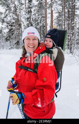 Donna che sciava con bambino in portatore di bambini Foto Stock