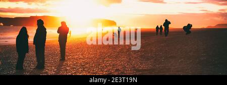 La gente silhouette camminare sulla spiaggia islandese viaggio estivo al tramonto flare. Folla di turisti che visitano la famosa attrazione islandese, Reynisfjara Black Foto Stock