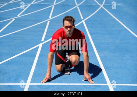 Atleta di runner che inizia a correre all'inizio della pista su piste da corsa blu all'aperto e allo stadio dei fiel. Sport e fitness man running in Foto Stock