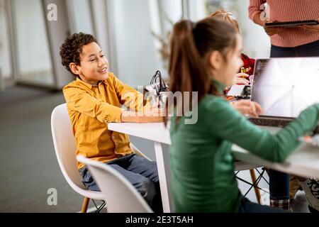 Smily African American insegnante di scienza femminile con gruppo di bambini programmazione di giocattoli e robot elettrici in classe robotica Foto Stock