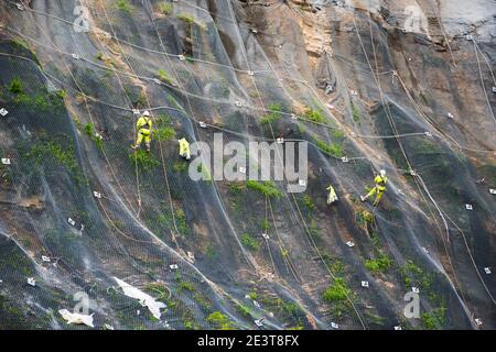 I lavoratori rinforzano il pendio della montagna con una rete metallica che impedisce la caduta di rockfall sulla strada. Hondarribia, Spagna. Informazioni generali astratte sul concetto di sicurezza Foto Stock