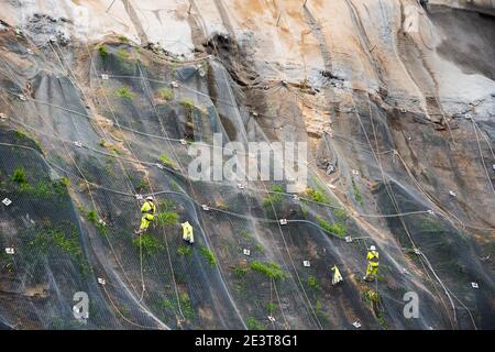 I lavoratori rinforzano il pendio della montagna con una rete metallica che impedisce la caduta di rockfall sulla strada. Hondarribia, Spagna. Informazioni generali astratte sul concetto di sicurezza Foto Stock