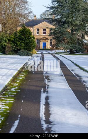 Un lungo e rettilineo percorso coperto di neve e giardino che conduce verso Una casa georgiana con una porta blu Foto Stock