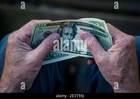 Uomo anziano che tiene in mano le fatture del dollaro USA, nota del dollaro 20 nella mano del pensionato Foto Stock