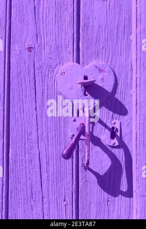 Vecchia porta in legno con serratura a forma di cuore e maniglia. Foto retrò viola. Apri il concetto del cuore. Amore, misericordia, idea di carità. Backgro d'epoca Foto Stock