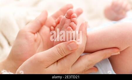 Closeup di donna che strofina delicatamente con la mano minuscoli piedi del suo neonato figlio con la pelle perfetta. Concetto di felicità della famiglia e genitori amorevoli con Foto Stock