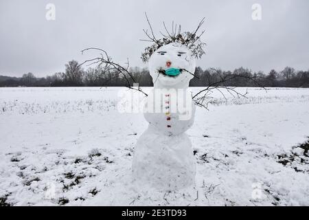 Pupazzo di neve divertente su campo nevoso che indossa una maschera medica contro il coronavirus, Covid-19 Foto Stock