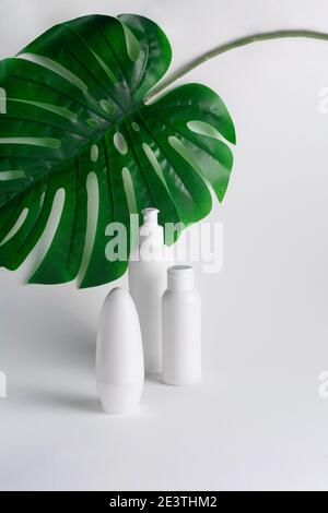 Set di prodotti cosmetici biologici per la cura del corpo su sfondo bianco con foglie tropicali. Crema, shampoo, balsamo, deodorante o sapone su flacone di plastica Foto Stock