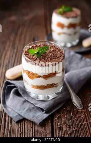 Classico caffè italiano senza forno dessert, delizioso tiramisù facile in un vaso, cosparso di polvere di cacao e trucioli di cioccolato su rustico backgrou di legno Foto Stock