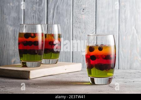 Dessert di gelatina con bacche in vetro su vecchio tagliere di legno, budino a strati dolce e colorato, fondo in cemento di pietra, vista angolare Foto Stock