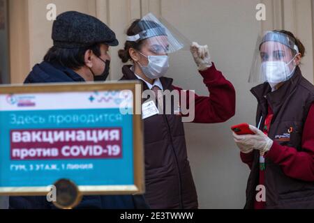 Mosca, Russia. 20 gennaio 2021 UNO staff che indossa una maschera aiuta i cittadini all'ingresso di un ufficio di vaccinazione COVID-19 teporary presso il grande magazzino GUM nel centro di Mosca, Russia. Dal gennaio 18, la Russia ha iniziato la vaccinazione di massa contro la nuova infezione da coronavirus COVID-19 con il vaccino Sputnik V. Il banner recita ''la vaccinazione COVID-19 è effettuata qui'' Foto Stock