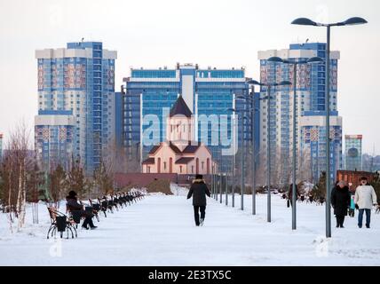 La gente riposa nel parco sullo sfondo della Chiesa armena e degli edifici residenziali in una serata invernale nuvolosa. Foto Stock