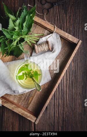 Sana bevanda medicinale, tè ortico in una tazza di vetro, decorato con foglie fresche su rustico sfondo di legno Foto Stock