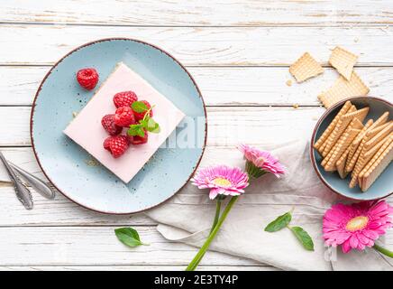 Delizioso dessert rinfrescante, senza cottura di barrette di cheesecake con lamponi dolci ricoperte di frutti di bosco freschi su sfondo bianco rustico in legno Foto Stock