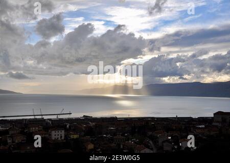 Il sole dietro le nuvole con raggi di luce che brillano sul mare. Raggi di sole che sbirciano attraverso le nuvole sul mare Adriatico di fronte Rijeka città, Croazia Foto Stock