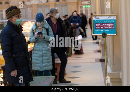 Mosca, Russia. Il 20 gennaio, 2021 cittadini che indossano maschere facciali rimangono in fila al di fuori di un'unità di vaccinazione mobile COVID-19 presso il grande magazzino GUM nel centro di Mosca, Russia. Dal gennaio 18, la Russia ha iniziato la vaccinazione di massa contro la nuova infezione da coronavirus COVID-19 con il vaccino Sputnik V. Il banner recita 'la vaccinazione COVID-19 è effettuata qui' Foto Stock