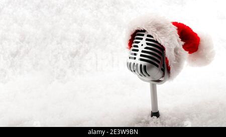 Concetto di musica natalizia e caroletti con un microfono che indossa una cappello di santa isolato su neve bianca con spazio di copia Foto Stock