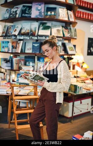 Libro di lettura della giovane donna con gli occhiali in Libreria Foto Stock