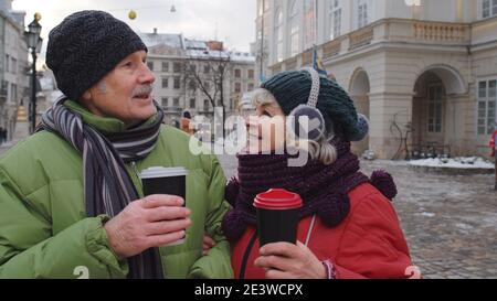 I turisti di moglie e marito che bevono dalle tazze, gustando il tè di bevanda calda, il caffè sulla strada centrale della città invernale a Lviv, Ucraina. Famiglia uomo e donna viaggio di vacanza attività. Vita dopo il pensionamento Foto Stock