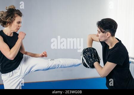 Primo piano di donna a piedi nudi gamba che pratica calci con taekwondo allenatore che tiene zampa di boxe. Scudo di boxe attivo concentrato per calci femmina con per Foto Stock