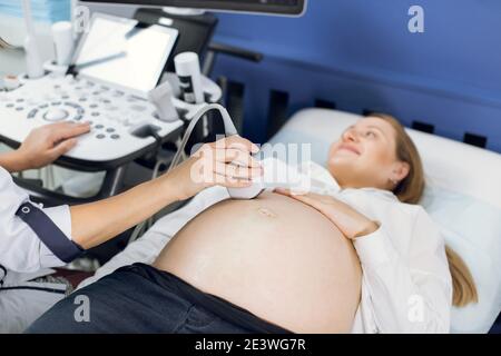 Primo piano delle mani del medico, utilizzando le moderne apparecchiature a ultrasuoni per lo screening della pancia di una donna incinta e premendo i pulsanti di un computer speciale Foto Stock