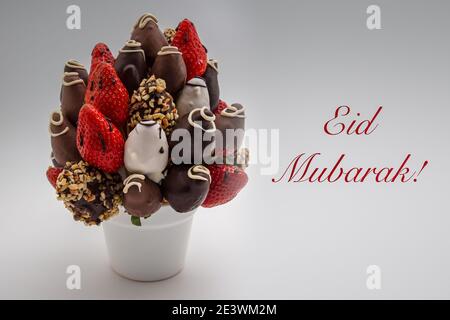 Biglietto d'auguri EID Mubarak con scritta rossa; un mazzo di fiori commestibili, arrangiamento di fragole ricoperte di cioccolato isolate su sfondo bianco Foto Stock