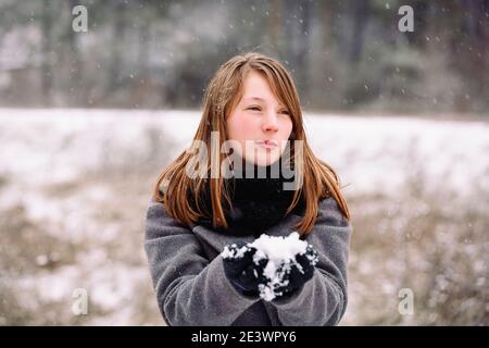 Una ragazza penosa tiene un globo di neve nelle sue mani e guarda al lato contro lo sfondo di una foresta innevata invernale. Foto Stock