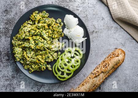 Uova strapazzate biologiche con spinaci in piastra su tavolo di marmo e pane Foto Stock