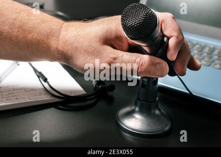 Una mano dell'uomo che ospita un piccolo microfono da tavolo prima di una conferenza virtuale. Stile moderno, concetto di comunicazione e conferenza. Foto Stock