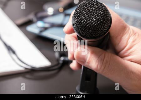 Una mano dell'uomo che ospita un piccolo microfono da tavolo prima di una conferenza virtuale. Stile moderno, concetto di comunicazione e conferenza. Foto Stock