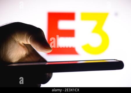 In questa illustrazione fotografica, una mano di una persona può contenere uno smartphone con il logo E3 (Electronic Entertainment Expo) visualizzato sullo sfondo. Foto Stock