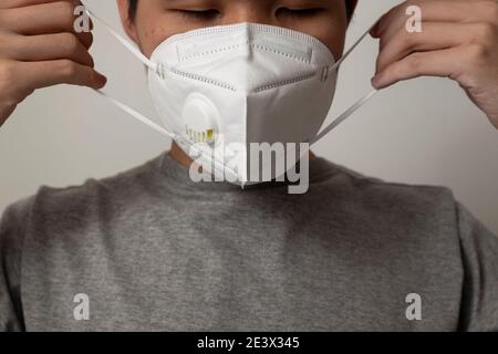 Uomo asiatico che indossa una maschera medica respiratoria N95 contro il Coronavirus (CoVID-19) e PM2,5 isolato su sfondo bianco. Passo dopo passo. Foto Stock