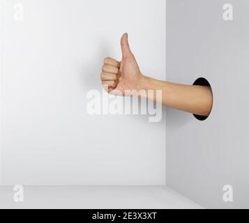 Mano umana con il pollice in su, che esce da un buco di carta. Foto Stock