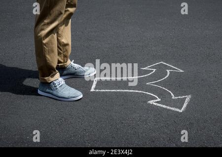 Giovane uomo in piedi su una strada con frecce che puntano in diverse direzioni concetto per le scelte di vita Foto Stock