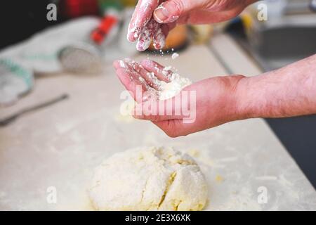 Primo piano le mani umane che fanno la pasta da pasta cruda / processo di preparazione del pane. Primo piano dell'impasto per impastare le mani dell'uomo. Foto Stock