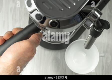 Vista dall'alto di una mano che tiene un manico portafiltro di una macchina da caffè mentre si prepara un caffè espresso. Il processo di preparazione di una bevanda aromatica mattutina. Foto Stock