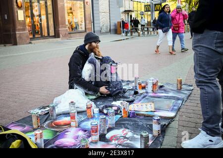 RIGA, LETTONIA - 4 MAGGIO 2020: Un artista di strada si trova in una piazza della città, fa soldi - disegna e vende i suoi dipinti Foto Stock