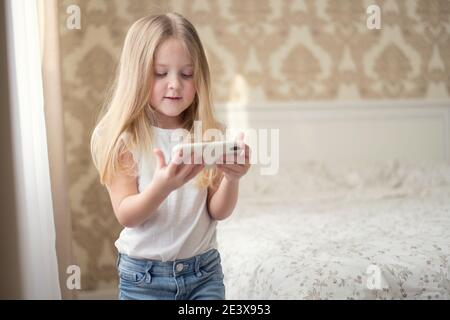 Una bambina di blondie stare con il telefono e gioca su giochi di social internet Foto Stock