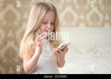 Una bambina di blondie stare con il telefono e gioca su giochi di social internet Foto Stock