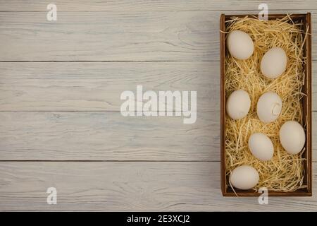 Una scatola di legno con paglia e sette uova di pollo si erge su uno sfondo di legno blu. La vista dall'alto e lo spazio vuoto per il testo Foto Stock