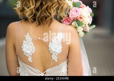 Retro della sposa in un primo piano vestito da sposa bianco. Bouquet di rose di sposa in colori pastello, ricci. Ali di angelo nella decorazione del vestito. BRI Foto Stock